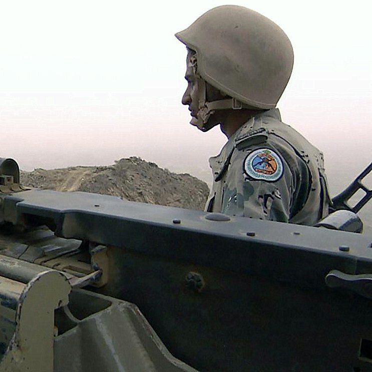 در این تصویر، یک سرباز در حال نشستن در کنار یک مسلسل سنگین دیده می‌شود. سرباز کلاه ایمنی بر سر دارد و به دوردست‌ها نگاه می‌کند. پس‌زمینه تصویر مه‌آلود به نظر می‌رسد و کوه‌ها یا زمین‌های ناهموار در دور دست قابل مشاهده است. سلاح در سمت چپ تصویر به وضوح دیده می‌شود و نشان‌دهنده‌ی آمادگی برای اقدام است. فضای تصویر به نوعی فضای نظامی و جدی را القا می‌کند.