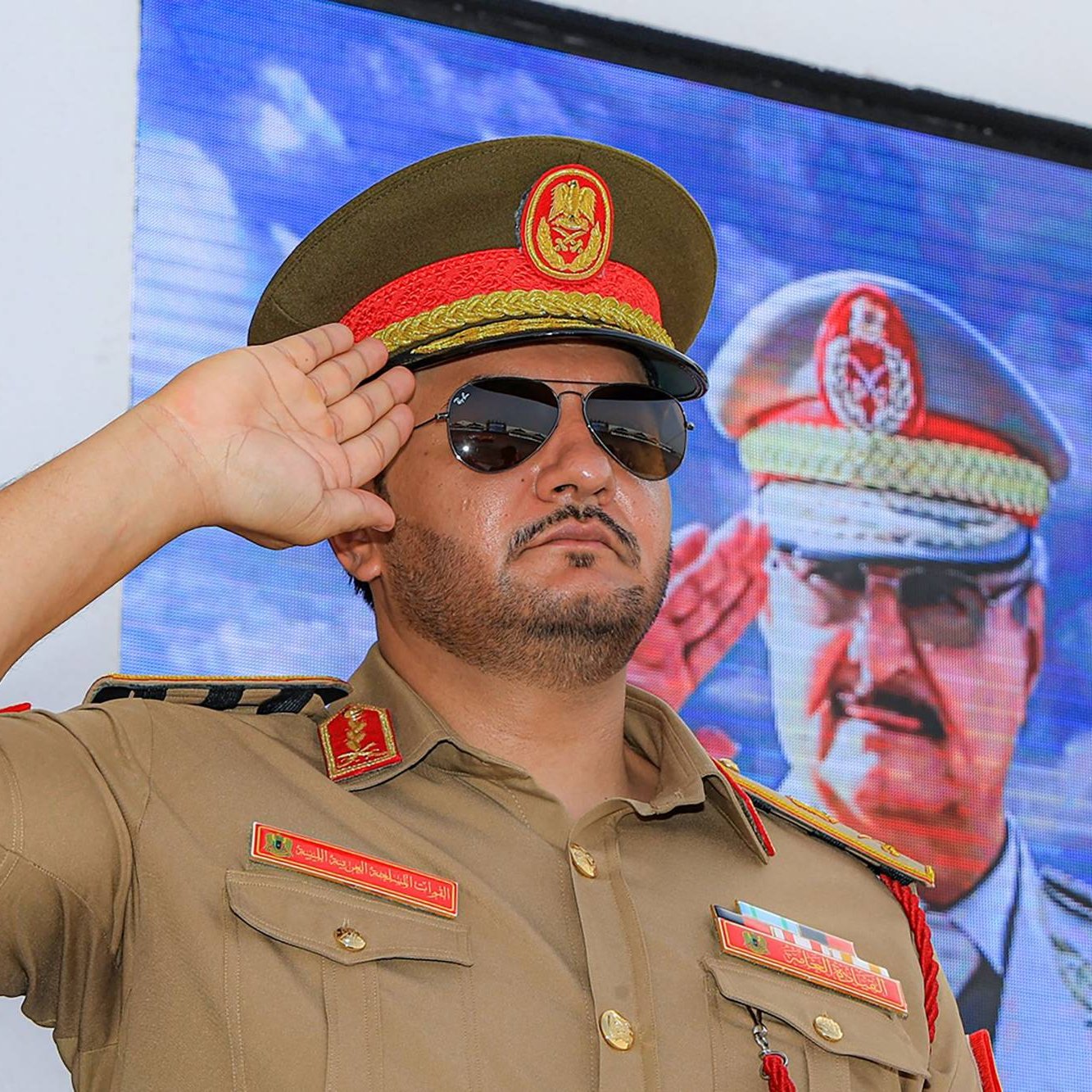 ضابط عسكري يرتدي زيًا رسميًا ونظارات شمسية، يؤدي تحية عسكرية.