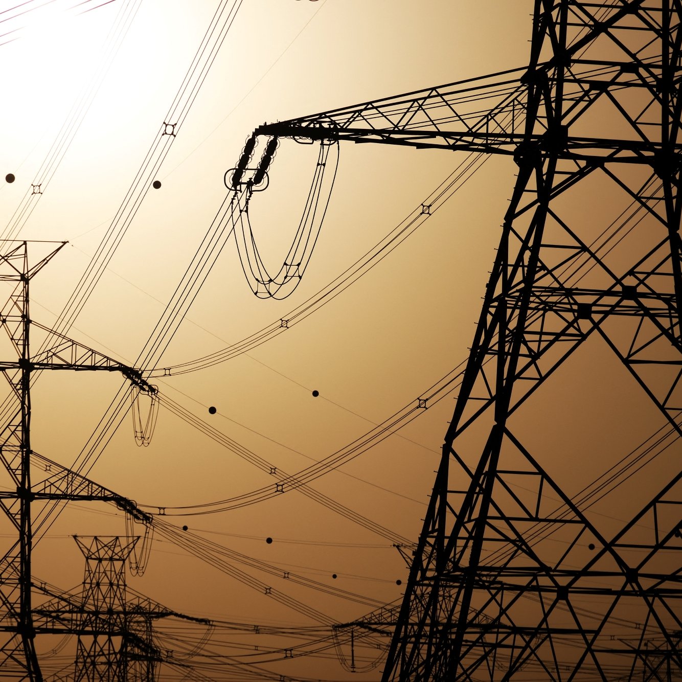 Silhouettes de pylônes électriques contre un ciel orangé.