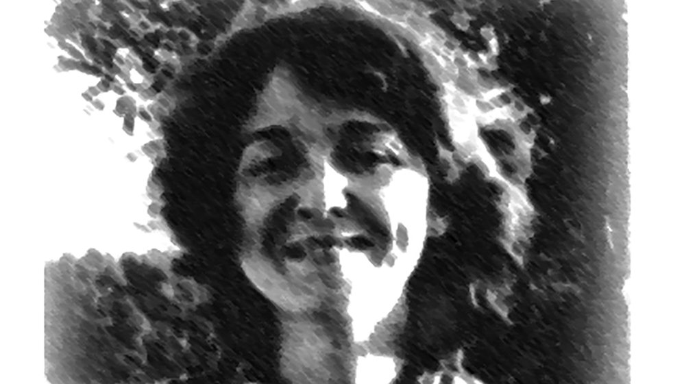 تصویر یک زن را نشان می‌دهد که با لبخند به دوربین نگاه می‌کند. او لباس گلداری با الگوهای مشخص پوشیده و موهای فر و لطیفی دارد. نور طبیعی از عقب او می‌تابد و باعث شده که تصویر حالتی نرم و هنری به خود بگیرد. پس‌زمینه نیز شامل درختانی است که جلوه‌ای زیبا به تصویر داده‌اند.