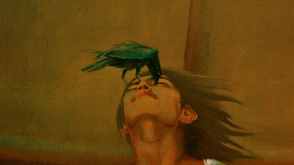 L'image représente un jeune homme dont la tête est légèrement inclinée en arrière. Il semble contemplatif, avec des cheveux longs flottant autour de son visage. Un oiseau noir, peut-être un corbeau, est posé sur son nez. Les couleurs de l'image sont sombres et un peu floues, créant une ambiance mystérieuse. Le fond a des nuances chaudes et brunes, ajoutant à l'aspect rêveur de la scène. L'ensemble évoque une interaction entre l'homme et l'oiseau, symbolisant peut-être une connexion ou une introspection.