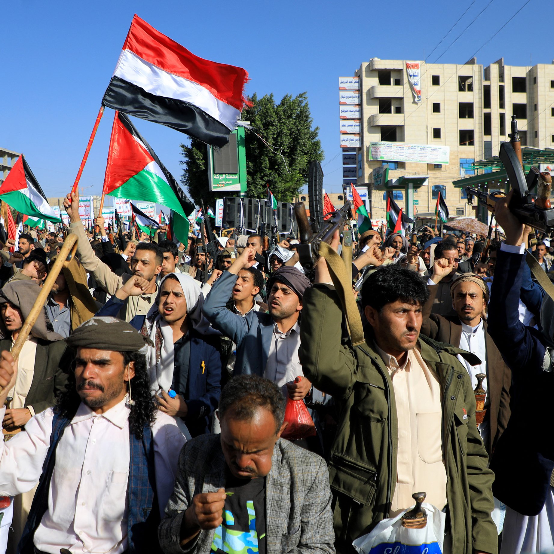 L'image montre une grande manifestation, probablement organisée par une foule, avec de nombreuses personnes levant des drapeaux, notamment des drapeaux aux couleurs de la Palestine. Les manifestants semblent déterminés et engagés, certains brandissant des banderoles. On peut voir des bâtiments en arrière-plan, suggérant un environnement urbain. L'atmosphère semble chargée d'énergie et de passion pour la cause.