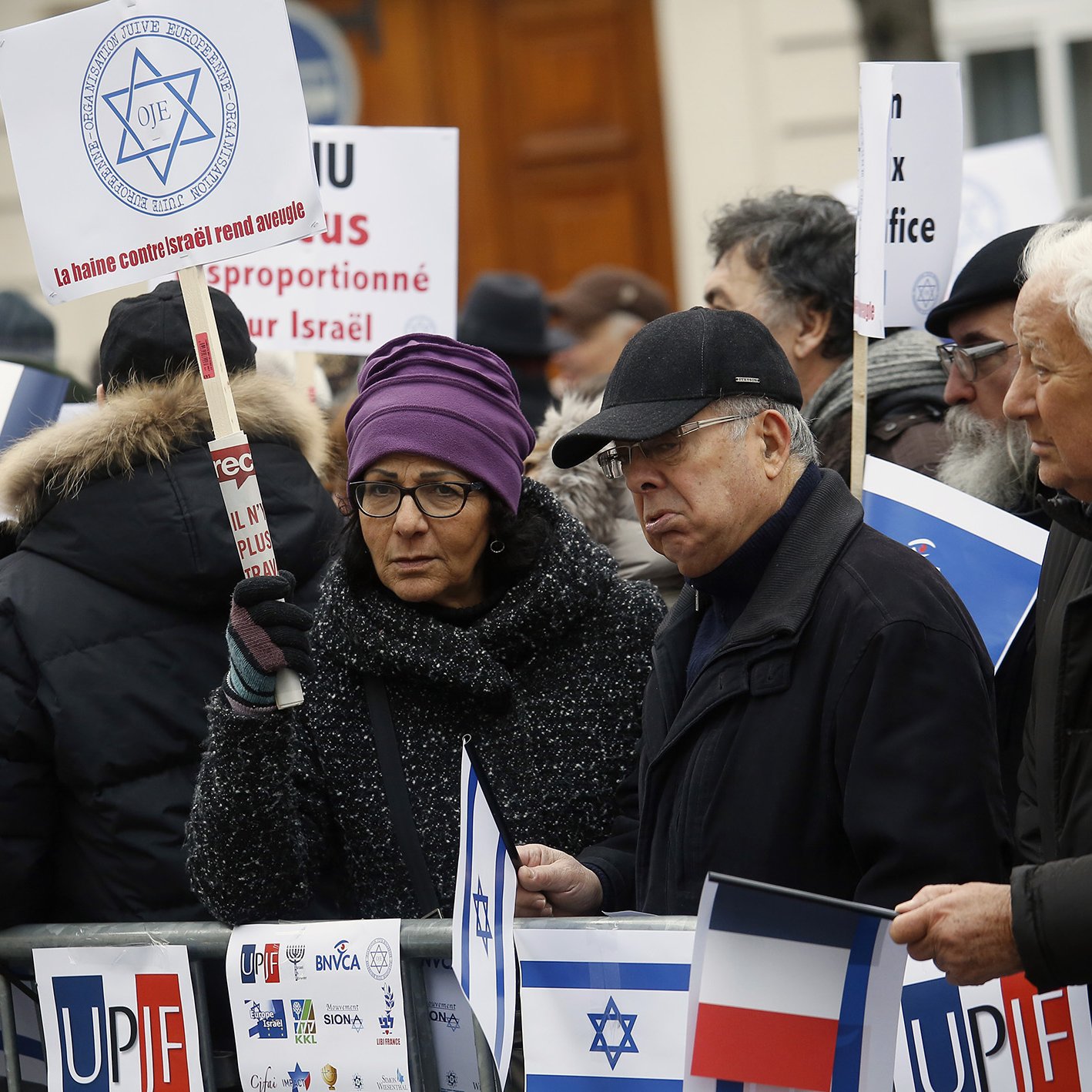 The image depicts a group of protesters gathered in an outdoor setting. They are holding signs and flags, including the Israeli flag and the French flag. The attendees appear to be engaged in a demonstration, showing solidarity or expressing opinions related to Israel. Some individuals are wearing winter clothing, suggesting it is during a colder season. The signs have various messages, possibly related to political or social issues concerning Israel. The atmosphere seems serious, highlighting a significant concern among the participants.