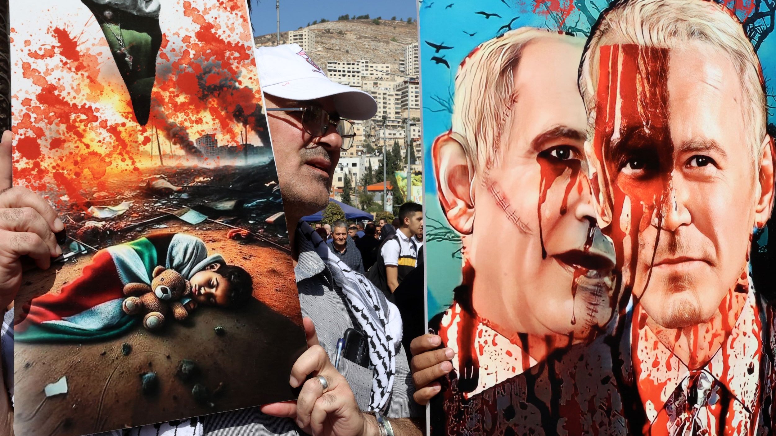 L'image montre des manifestants tenant des pancartes lors d'une démonstration. À gauche, une affiche illustre une scène tragique avec un enfant couché sur le sol, entouré de débris et d'une atmosphère de destruction. À droite, une illustration satirique ou critique représente deux figures, avec des visages peints évoquant des thèmes de violence, symbolisés par des éclaboussures de sang. L'ensemble évoque des questions politiques et humanitaires, avec un fort impact visuel.