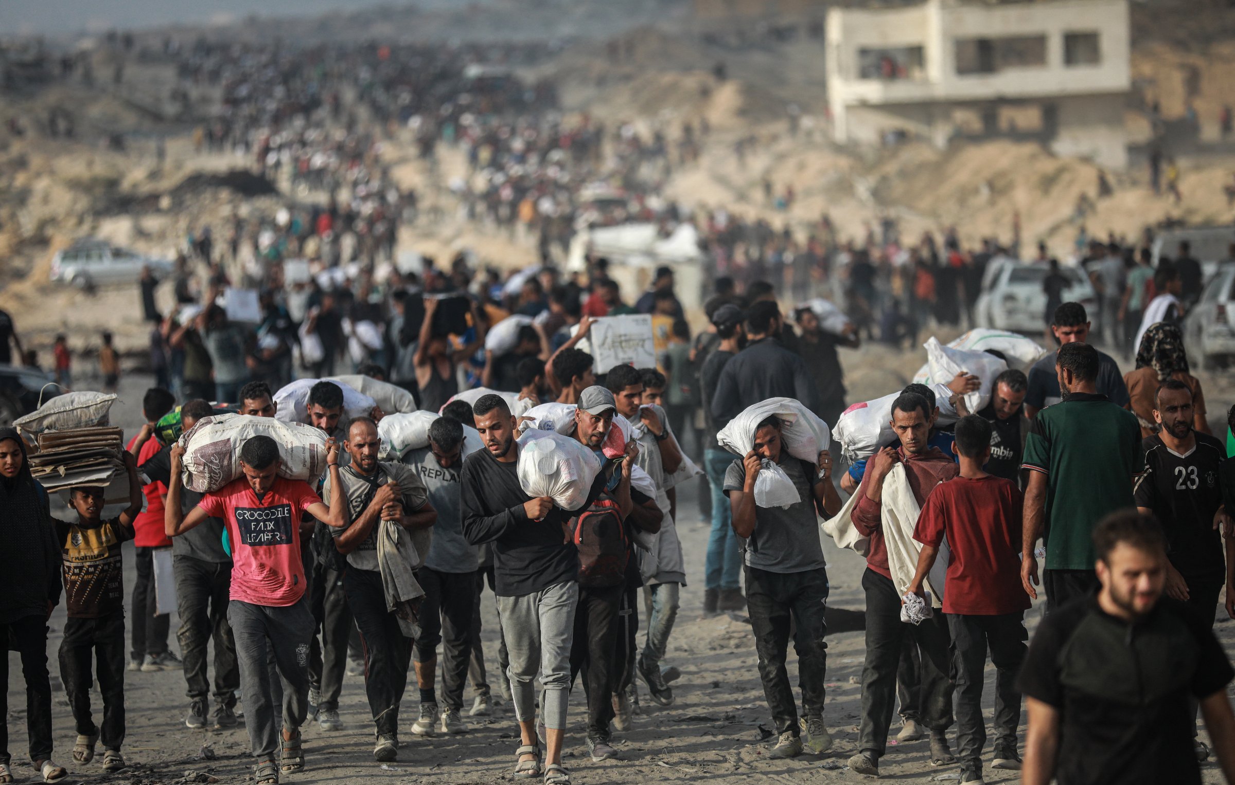 Un grupo de personas camina por un terreno árido, llevando sacos y luciendo cansados.