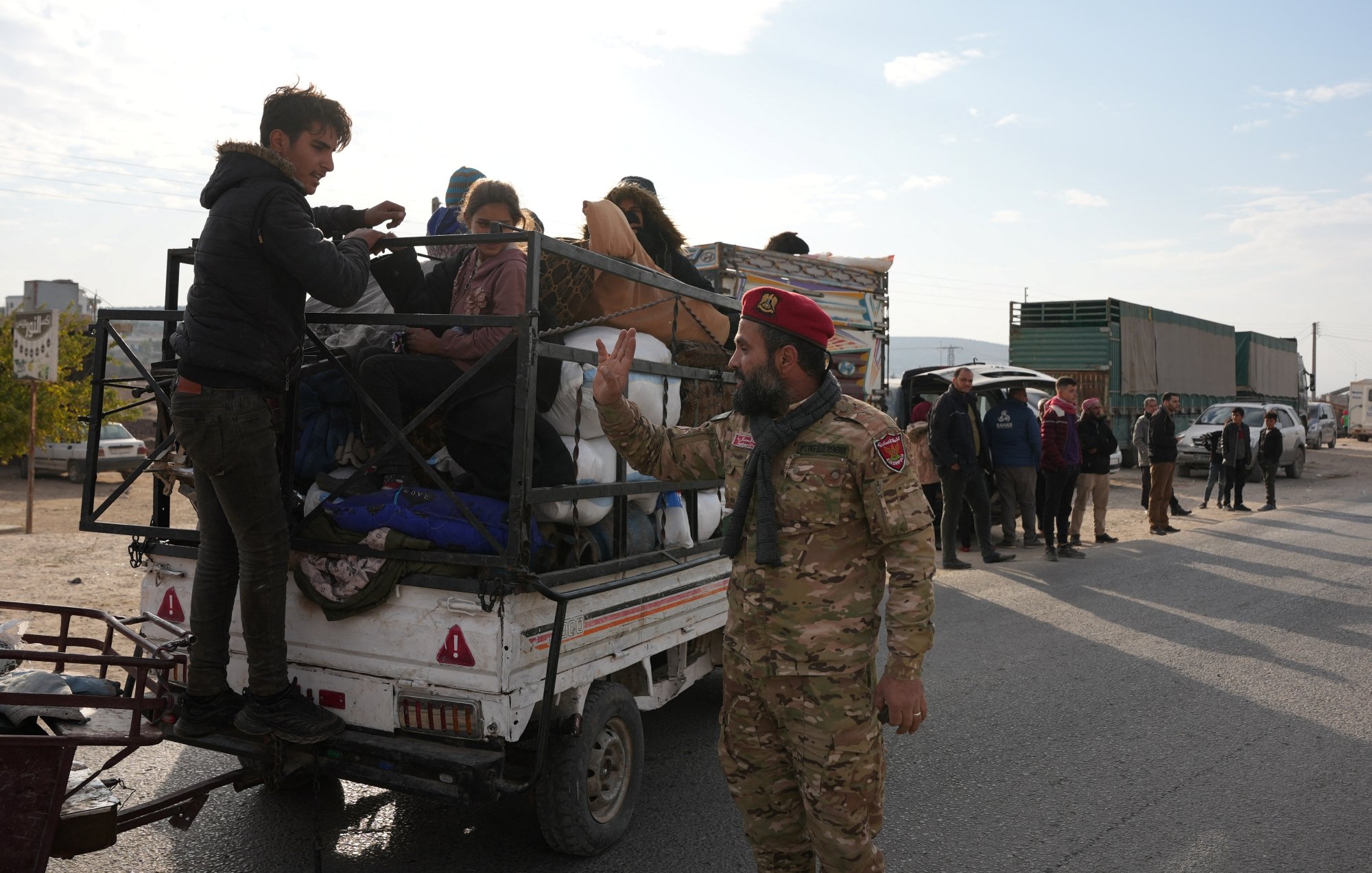 Des personnes sur une camionnette, un soldat gesticule au sol. Atmosphère tendue.