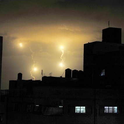 L'image montre un ciel nocturne illuminé par des éclairs, avec des nuages sombres en arrière-plan. On peut voir des bâtiments en silhouette, avec des fenêtres lumineuses qui créent un contraste avec l'obscurité environnante. Les éclairs apparaissent comme des points lumineux dans le ciel, ajoutant une atmosphère dramatique à la scène.
