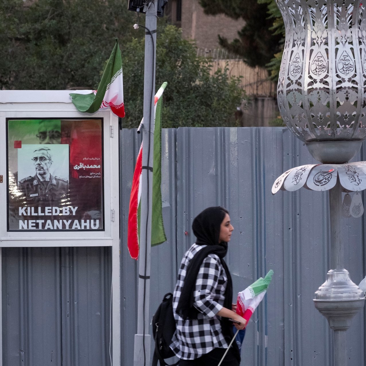 Deux affiches de victimes avec le texte "Killed by Netanyahu", une femme passe avec un drapeau.