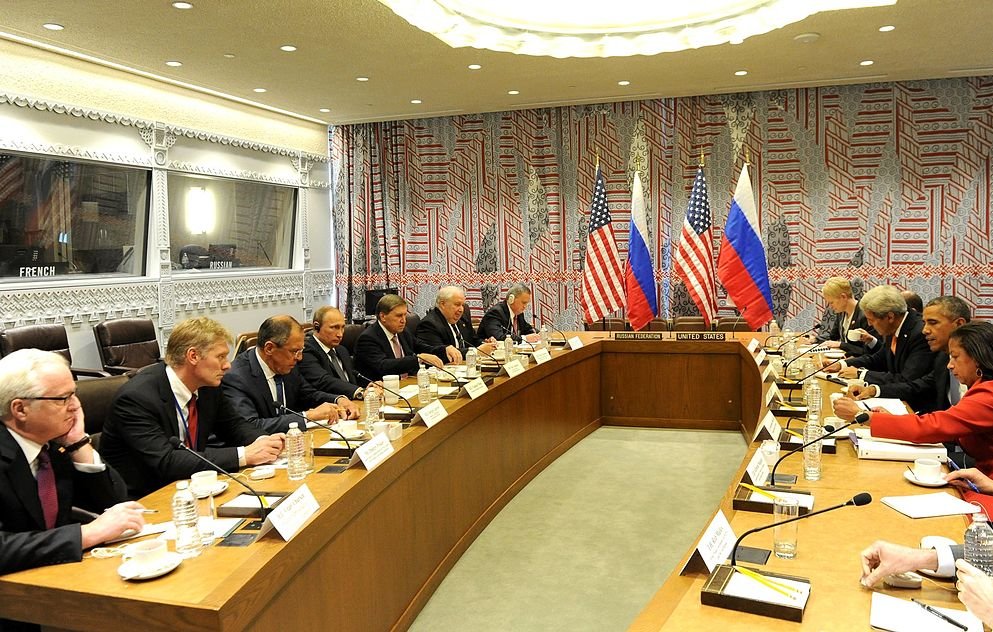تظهر في الصورة مجموعة من المسؤولين في قاعة اجتماعات. الجانبان يمثلان الولايات المتحدة وروسيا، مع وجود علمي كلا البلدين على الطاولة. يبدو أن الاجتماع يتناول قضايا دبلوماسية أو سياسية هامة. الطاولة طويلة، وهناك عدد من الكراسي المحيطة بها، حيث يجلس المشاركون يتبادلون النقاشات. تظهر ملامح الجدية والتركيز على وجوههم، مما يدل على أهمية الحوار الجاري. الديكور الخلفي للمكان يتضمن تصاميم حديثة.
