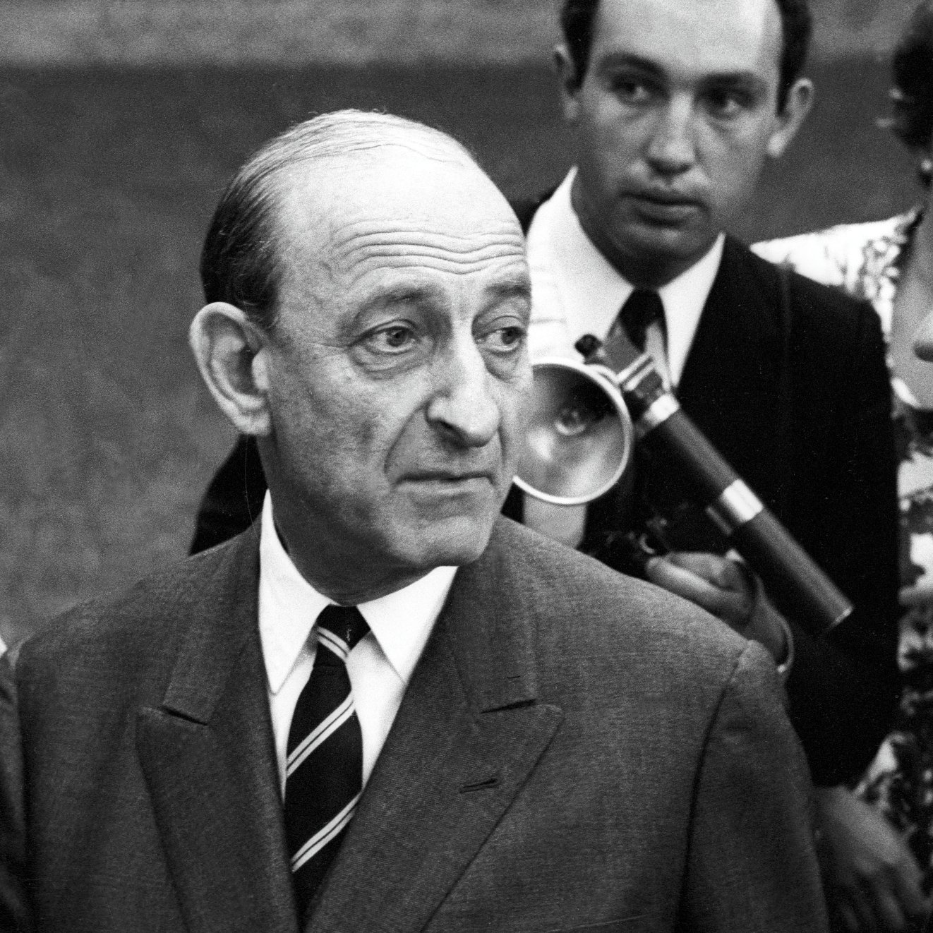 Deux hommes en costume, discutant sérieusement, entourés d'autres personnes. Époque rétro.