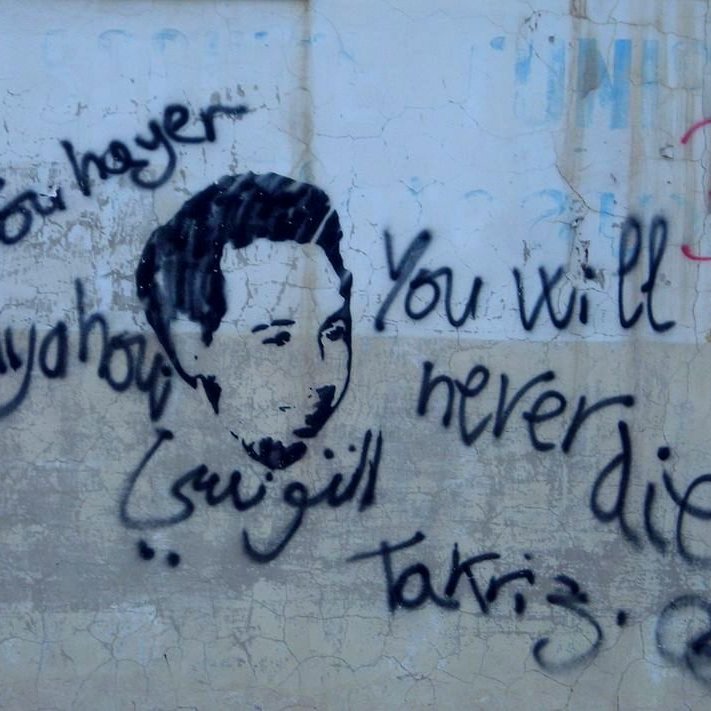 تظهر الصورة رسمًا على جدار يظهر وجه شخص، محاطًا بعبارات مكتوبة بخط يدوي. من بين هذه العبارات، تُظهر باللغة الإنجليزية "You will never die" (لن تموت أبدًا) وفي اللغة العربية "يحيى" و"تقديس". يبدو أن العمل يعبر عن رسالة تعاطف أو تأبين، مع تداخل بين الثقافات واللغات في الكتابة.