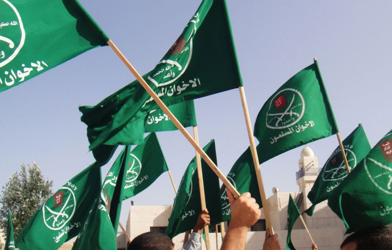 L'image montre un groupe de personnes brandissant des drapeaux verts. Les drapeaux portent probablement des symboles ou des inscriptions en arabe, ce qui suggère un contexte politique ou religieux. L'environnement semble être en extérieur, possiblement lors d'un rassemblement ou d'une manifestation.