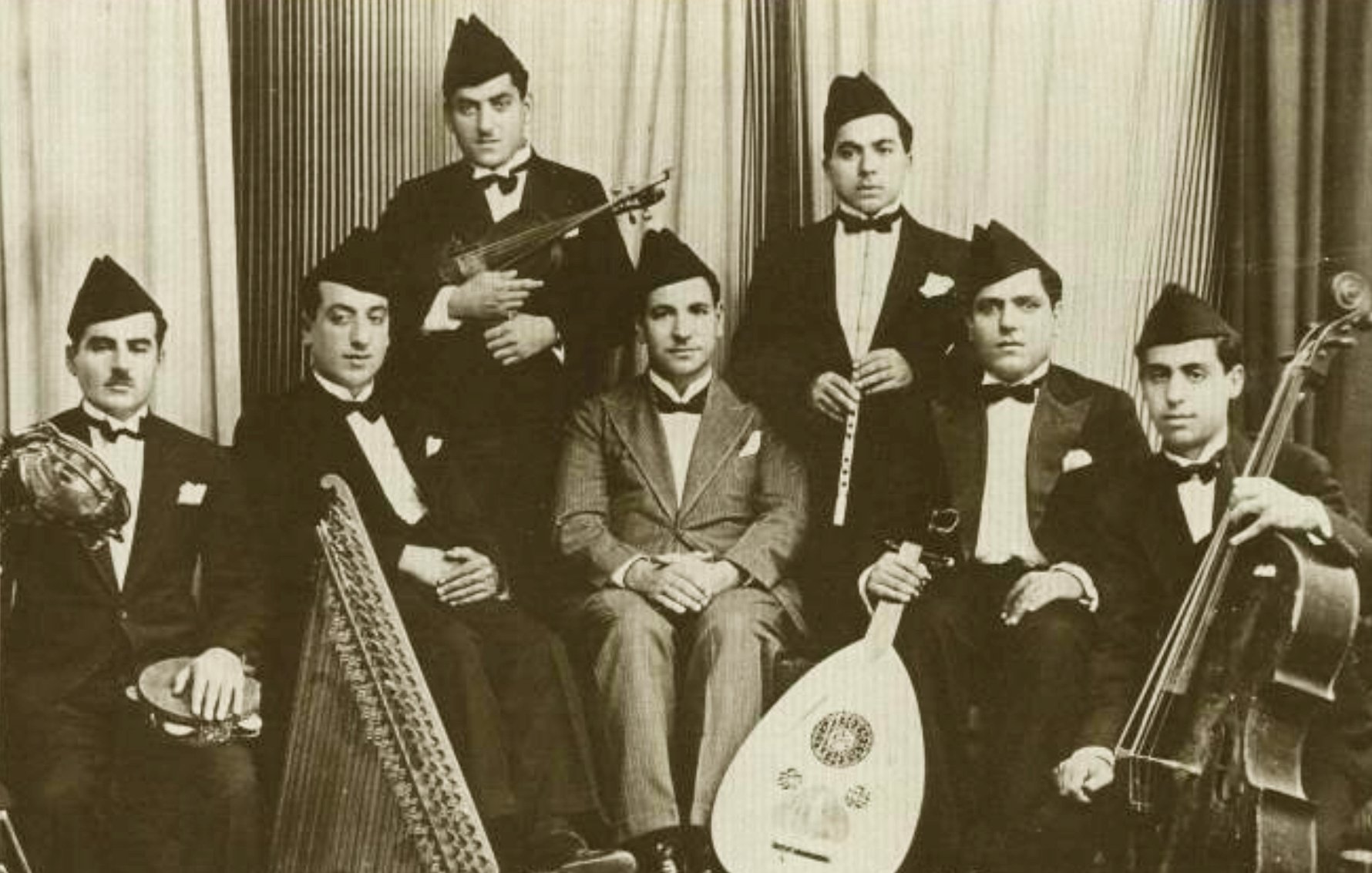 Groupe de musiciens en costume noir, instruments variés, ambiance d'époque.