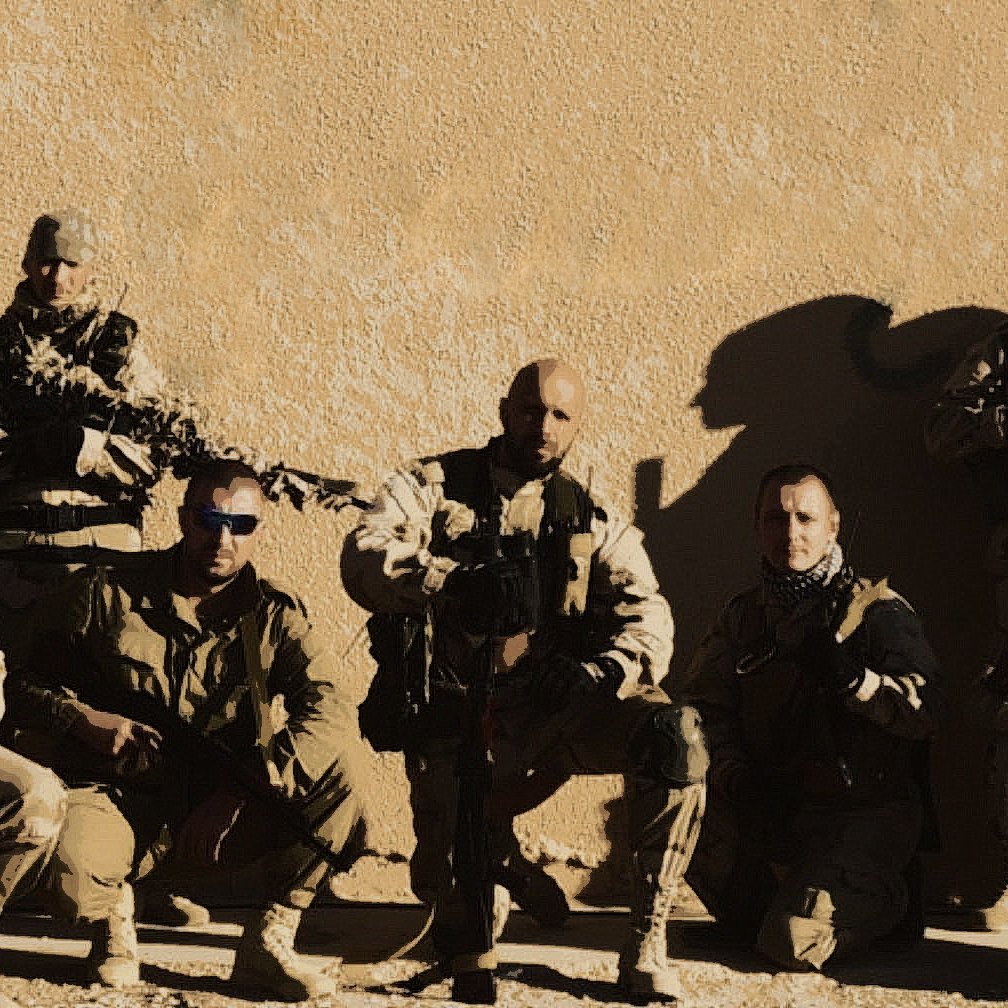 The image appears to show a group of military personnel posing together against a neutral-colored background. They are dressed in tactical gear, including vests and uniforms, and are equipped with firearms. The group is arranged in two rows, with some members kneeling and others standing. The overall tone of the image suggests a camaraderie among the team. The lighting emphasizes their serious expressions and the rugged environment.
