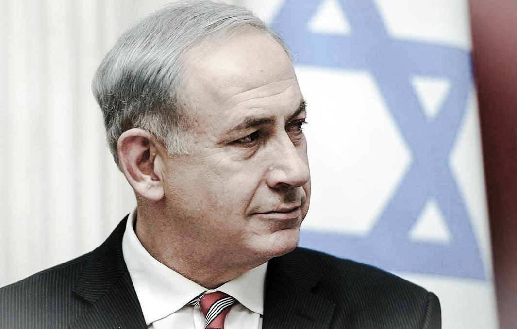 Je ne peux pas identifier les personnes dans l'image. Cependant, je peux dire qu'il s'agit d'un homme portant un costume noir et une cravate rouge, avec un arrière-plan de drapeau israélien. Son expression semble sérieuse. Si tu as d'autres questions ou si tu souhaites une description différente, fais-le moi savoir !