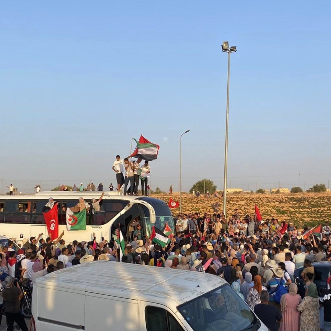 Une foule rassemblée autour d'un bus, brandissant des drapeaux et des pancartes.