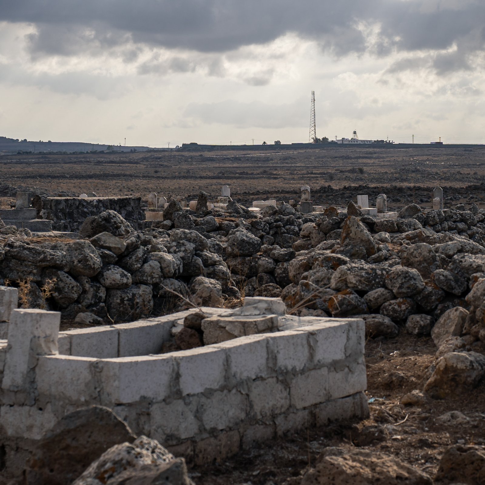 Un paysage aride avec des tombes et des pierres, sous un ciel nuageux.