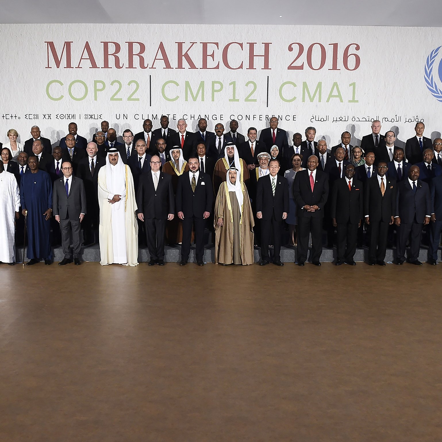 L'image montre un groupe de participants rassemblés lors de la conférence COP22 qui s'est tenue à Marrakech en 2016. Les membres représentés incluent des dirigeants et des délégués de divers pays, vêtus de costumes formels et de tenues traditionnelles. Ils se tiennent debout sur des gradins, souriant pour la photo officielle, avec un fond affichant le nom de l'événement et des logos des Nations Unies. L'ambiance évoque un sentiment de collaboration internationale pour faire face aux défis climatiques.