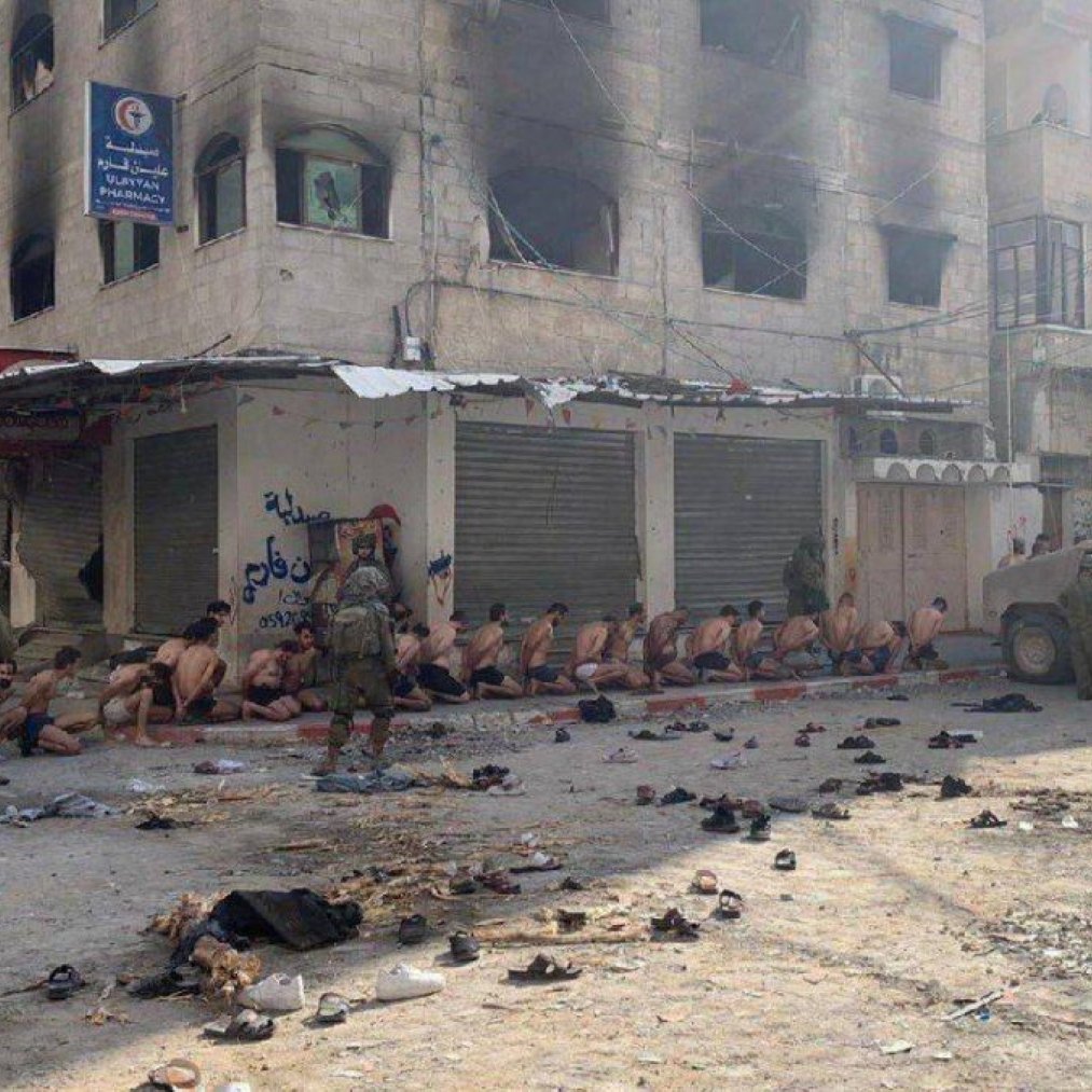 Scène de rue sombre avec des personnes assises et des soldats armés. Atmosphère tendue.