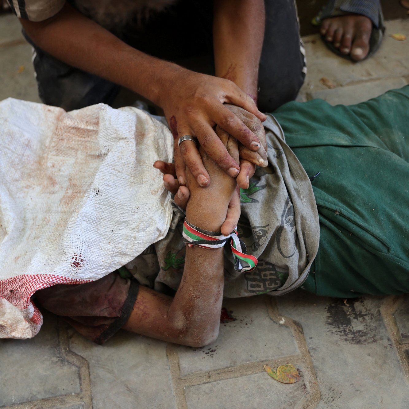 A person lying on the ground, covered in a cloth, with another person holding their hand.