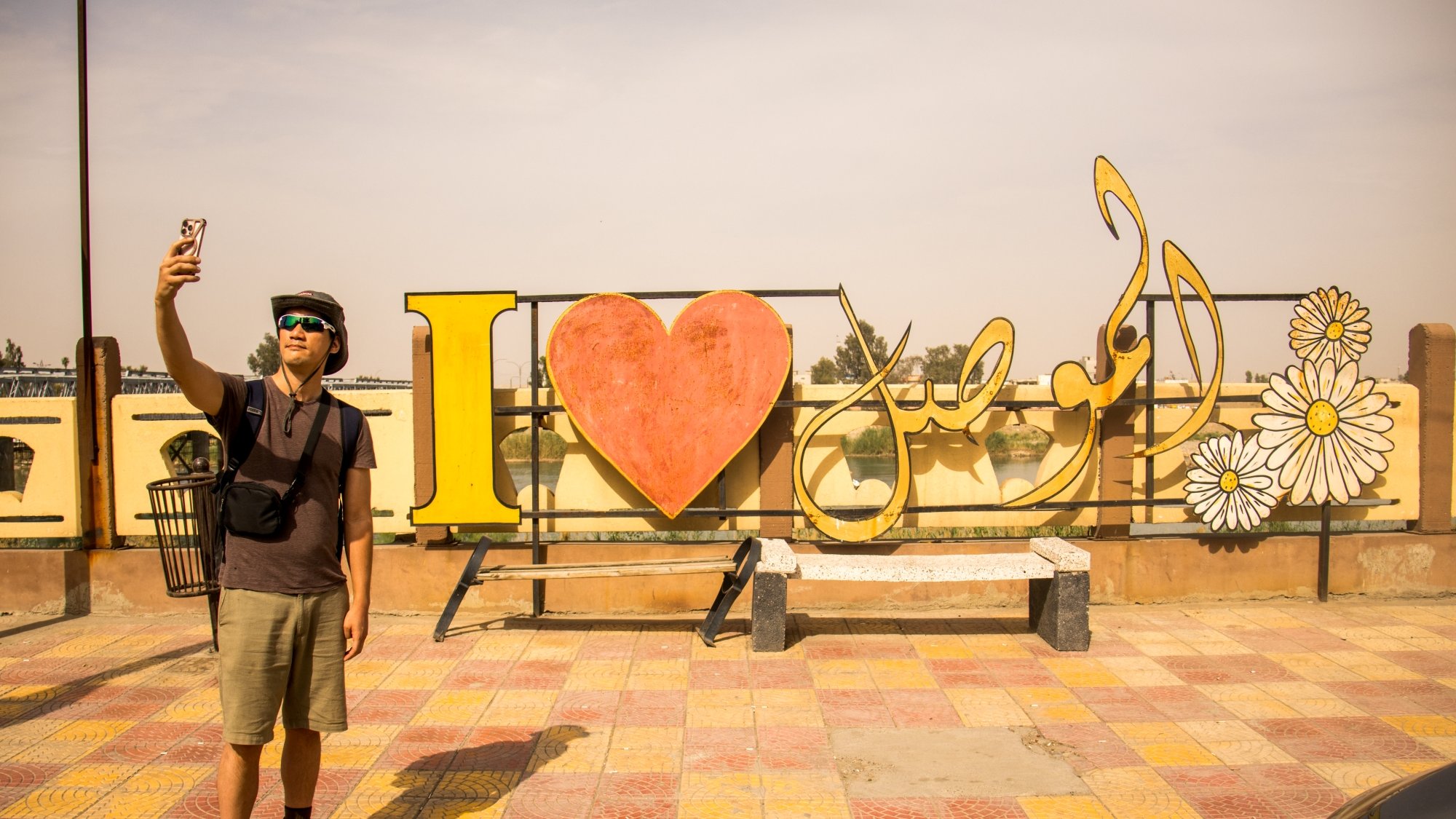 Un homme prend un selfie devant une grande inscription colorée "I ❤️ [nom]".