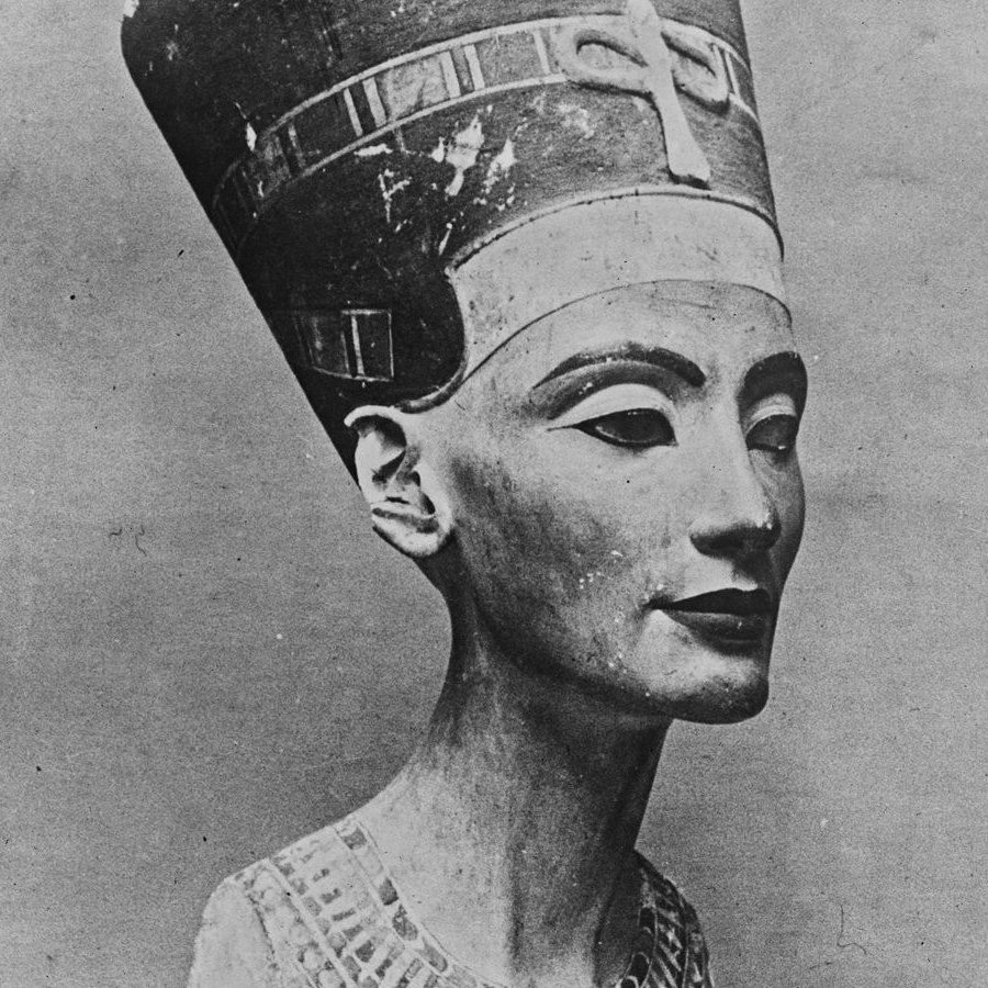 L'image montre un buste sculpté d'une femme portant une couronne élevée et un collier élaboré. Ce buste est souvent associé à la célèbre reine égyptienne Néfertiti. Les traits du visage sont raffinés et symétriques, avec des yeux en amande et des lèvres délicates. La couronne est ornée de motifs distinctifs, et le collier est décoré de détails géométriques. L'œuvre fait partie de l'art égyptien ancien, symbolisant la beauté et l'élégance de l'époque.