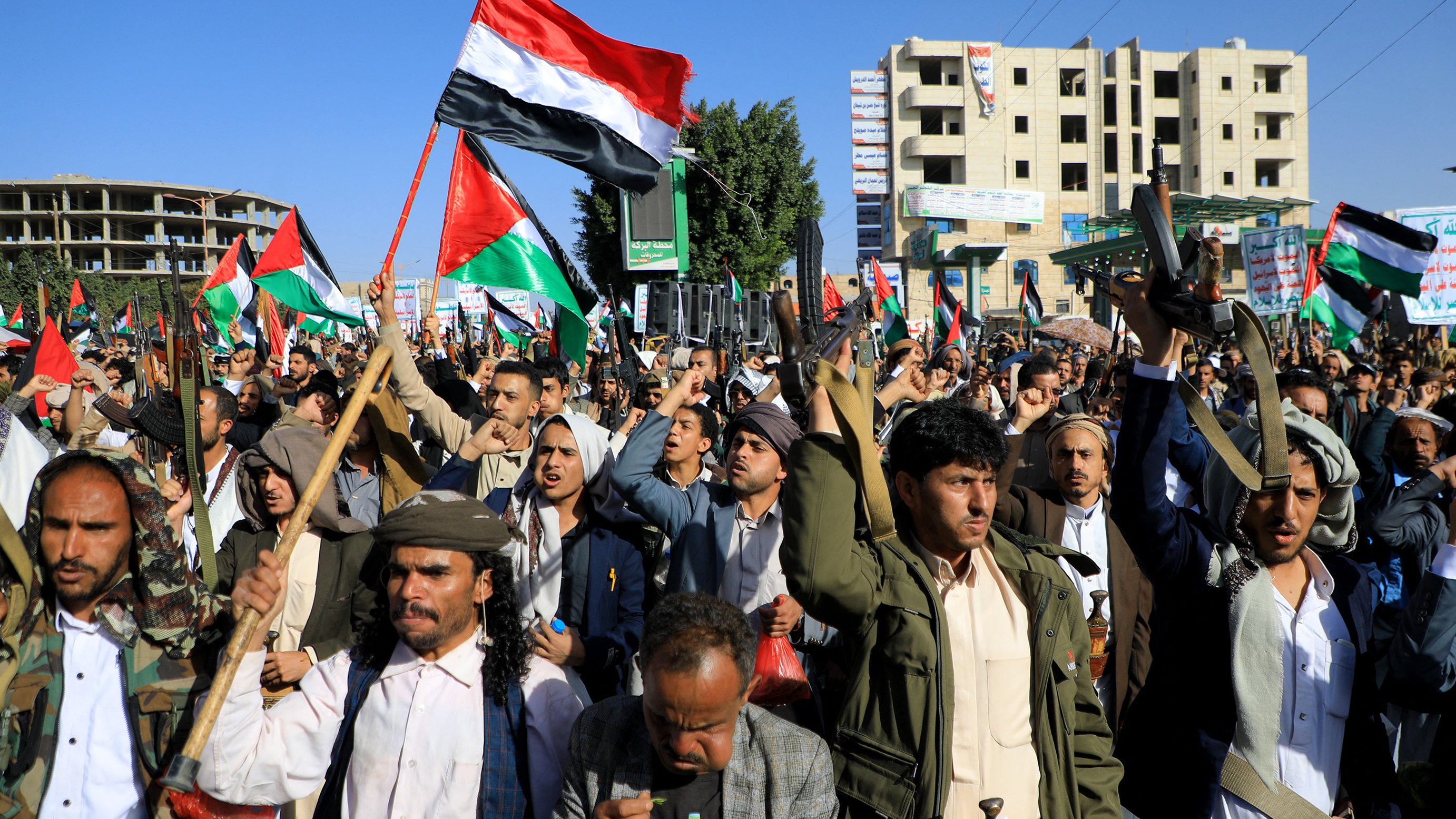 تظهر الصورة مجموعة من الأشخاص في تظاهرة حاشدة، يحملون الأعلام ويرتدون زيًّا تقليديًا. تعبر الوجوه عن الحماس وتظهر الأعلام التي تحمل ألوان الوطن. تتواجد خلفهم بنايات وبعض العلامات التجارية، مما يوحي بأن المكان هو منطقة حضرية. يبدو أن المتظاهرين يمارسون حقهم في التعبير عن آرائهم والمشاركة في حدث سياسي أو اجتماعي.