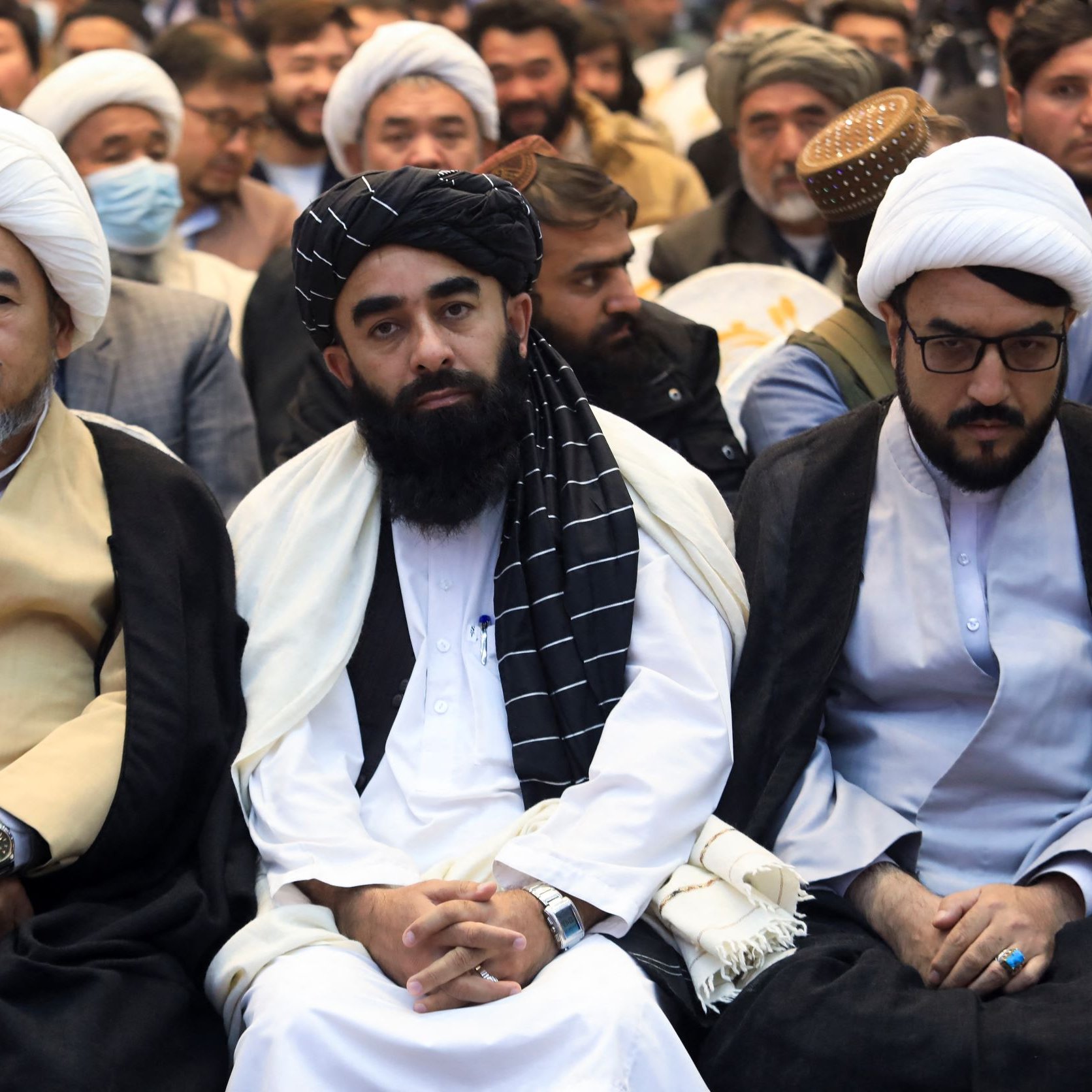 نگاهی به تصویر، گروهی از مردان را می‌بینیم که در یک مراسم نشسته‌اند. در این تصویر، سه نفر در جبهه جلو مشخص‌تر هستند. آنها لباس‌های سنتی خود را پوشیده‌اند و ظاهر آنها نشان‌دهنده تعلقات مذهبی و فرهنگی‌شان است. برخی از حضار در پس‌زمینه نیز قابل مشاهده هستند و به نظر می‌رسد این جمع در حال شرکت در یک برنامه خاص یا مراسم مذهبی هستند. فضای کلی عکس جدی و رسمی به نظر می‌رسد.