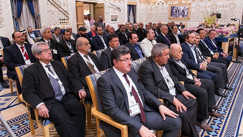 L'image montre un groupe de personnes assises, probablement lors d'une réunion ou d'une conférence. Ils semblent être des hommes d'affaires ou des responsables, vêtus de costumes formels. L'arrière-plan est orné de décorations élégantes, typiques d'une salle de conférence dans un cadre sophistiqué. Les participants regardent attentivement, suggérant un moment de discussion ou de présentation importante.