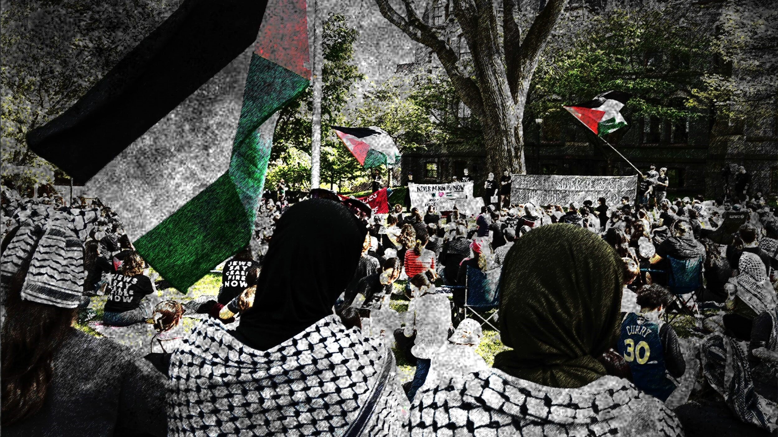 L'immagine mostra una manifestazione in cui partecipano molte persone, alcune delle quali indossano sciarpe tradizionali palestinesi. Si possono vedere delle bandiere palestinesi sventolare sullo sfondo. La scena è caratterizzata da una grande affluenza di partecipanti, con un'atmosfera di attivismo e solidarietà. Gli alberi e l'architettura circostante forniscono un contesto urbano alla manifestazione, suggerendo un forte impegno per una causa sociale.