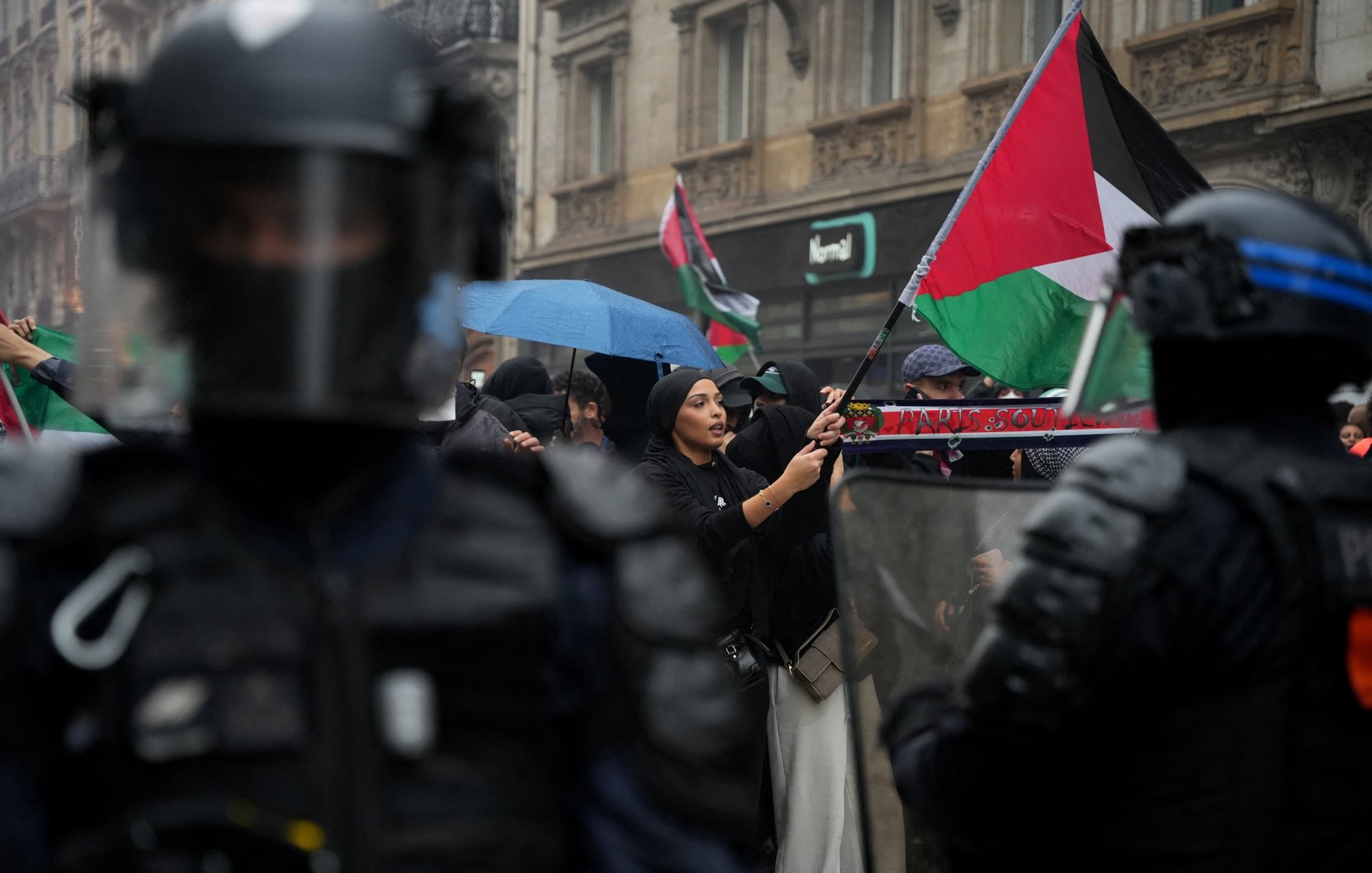 Manifestation avec des drapeaux palestiniens, policiers en tenue anti-émeute, ambiance tendue.