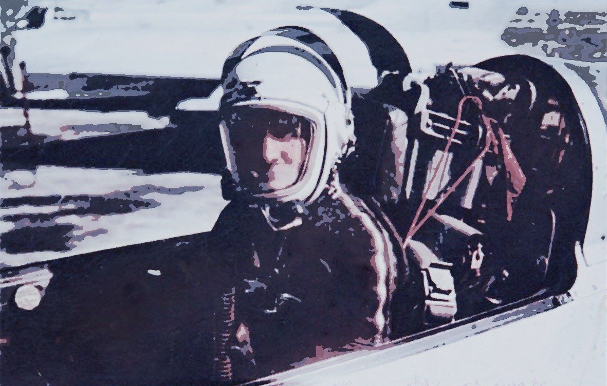 L'image montre un pilote assis dans le cockpit d'un avion ou d'un vaisseau spatial. Il porte un casque de protection et une combinaison, ce qui indique qu'il est probablement en préparation pour un vol. Le décor autour de lui semble être un environnement aéroporté ou une piste de lancement. L'ambiance de l'image évoque la technologie et l'exploration aérienne ou spatiale.