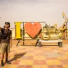 Un homme prend un selfie devant une grande inscription colorée "I ❤️ [nom]".