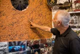 Un homme touche un mur orangé couvert de signatures et de photos souvenirs.