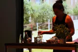 Una donna versa acqua in un bicchiere accanto a piante aromatiche su un tavolo.