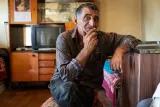 Un homme pensif, assis dans une pièce sobre, entouré de meubles simples.