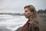 Femme au bord de la mer, cheveux blonds, regard contemplatif vers l'horizon.