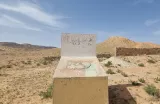 Un monolithe décoloré au milieu d'un paysage désertique et vallonné.