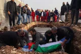 L'image montre un groupe de personnes rassemblées autour d'une tombe. Des hommes portent un cercueil recouvert d'un drapeau. L'ambiance est solennelle, et des figures sont visibles en arrière-plan, observant la scène.