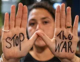 Femme tenant ses mains ouvertes, écriture sur les paumes : "STOP" d'un côté, "THE WAR" de l'autre.