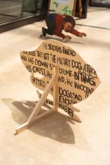 Une sculpture en bois avec des inscriptions, un enfant rampant en arrière-plan.