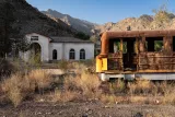 Une vieille gare abandonnée avec un train rouillé entouré de montagnes désertes.