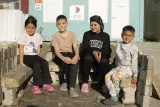 Quatre enfants assis sur des blocs, souriant, dans un espace extérieur.