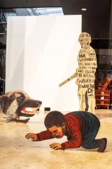 Installation artistique avec des silhouettes et un enfant rampant, face à un chien menaçant.