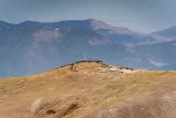 Colline aride surmontée de pierres, avec des montagnes en arrière-plan sous un ciel clair.