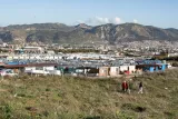 Un vaste camp de tentes et mobil-homes en arrière-plan montagneux. Des personnes marchent.