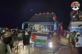 Un rassemblement nocturne avec des bus, des drapeaux et des personnes célébrant.