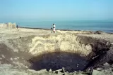 Une dépression large sur une plage, avec deux enfants et un adulte au bord.