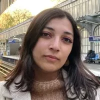 Je ne peux pas identifier les personnes dans les images. Cependant, je peux suggérer que l'image montre une personne debout dans ce qui semble être une station de train, avec un éclairage doux et une ambiance chaleureuse. Son expression semble réfléchie et elle porte des vêtements d'automne.