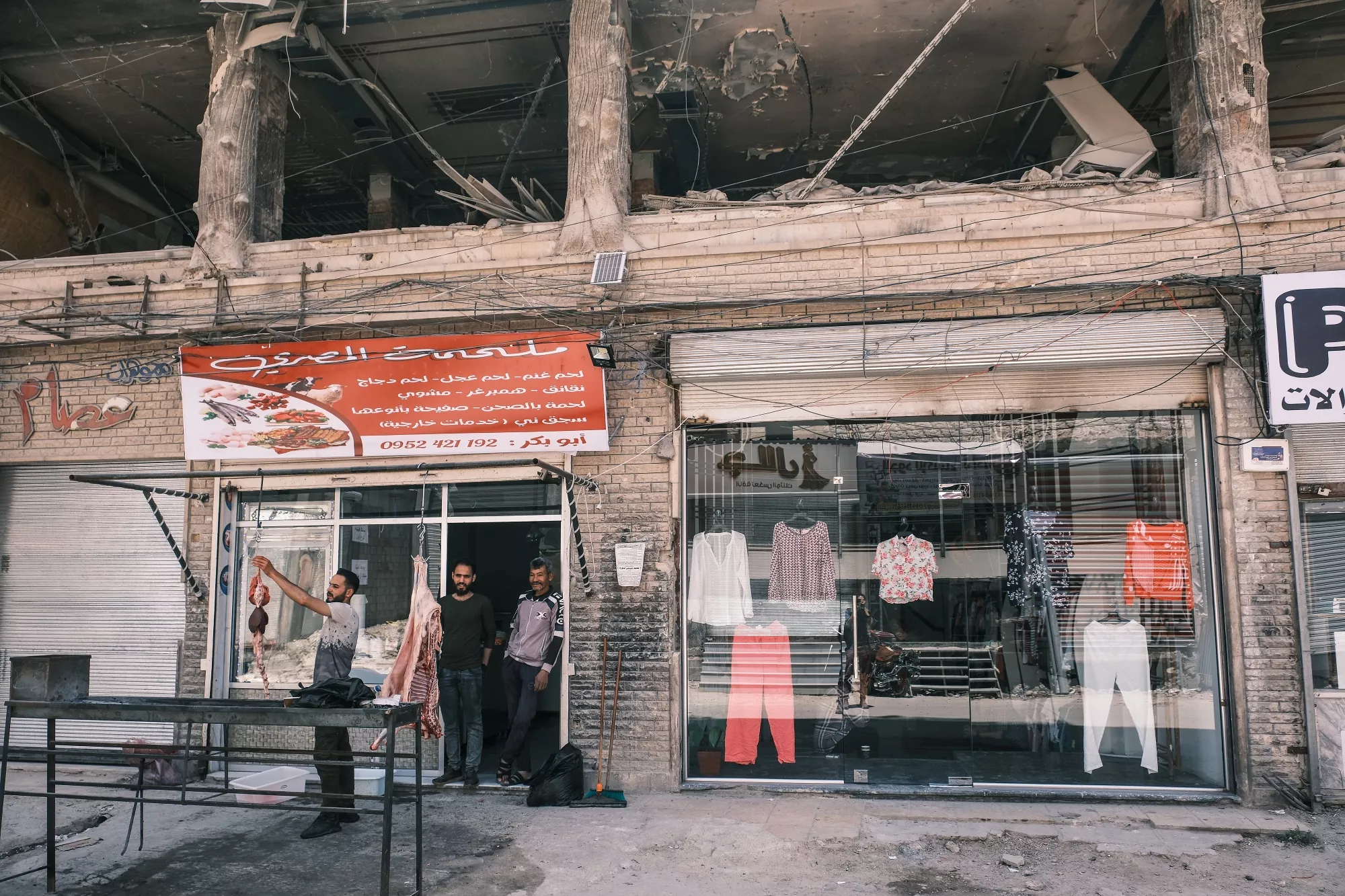 Davanti a un negozio di abbigliamento danneggiato, tre uomini stanno parlando sotto un'insegna.